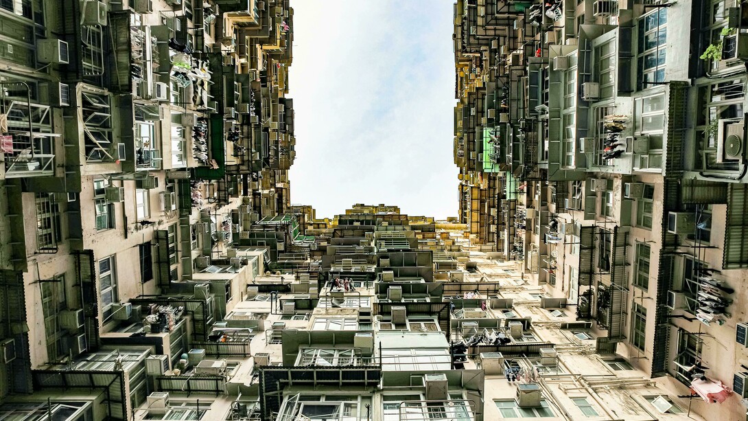 Low-angle view of a towering residential building in Hong Kong, reflecting the stark contrast between urban density, inequality, and poverty