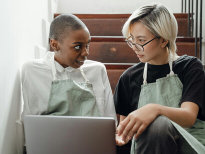 Colleagues in aprons sitting on a staircase, browsing social media on computer    