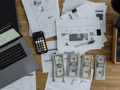 The table holds an arrangement of papers, a calculator, coins, and various investment instruments