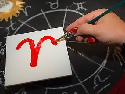 Female astrologer aries draws zodiac sign on white tile