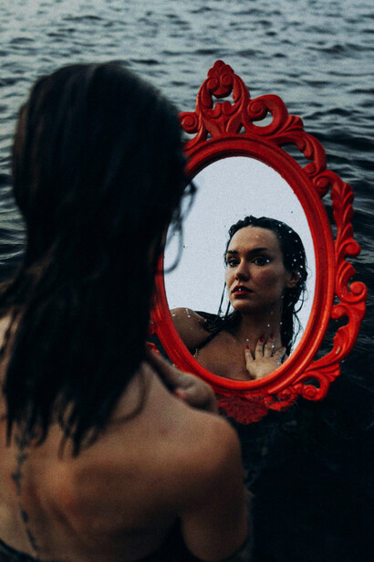 A woman in a bathing suit facing the sea as her reflection appears in the water