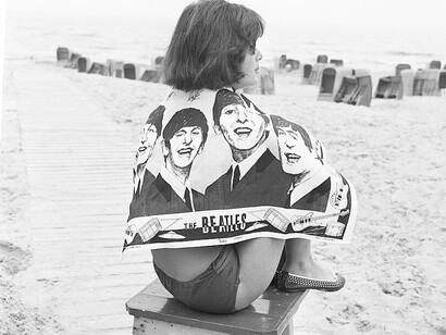 La musica dei Beatles arriva oltreoceano a partire dalla metà degli anni Sessanta, una ragazza in spiaggia indossa un telo mare con il volto della band