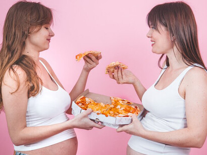 Expecting mothers eating pizza by a pink wall, representing the potential health risks of consuming Western diet and processed foods during pregnancy