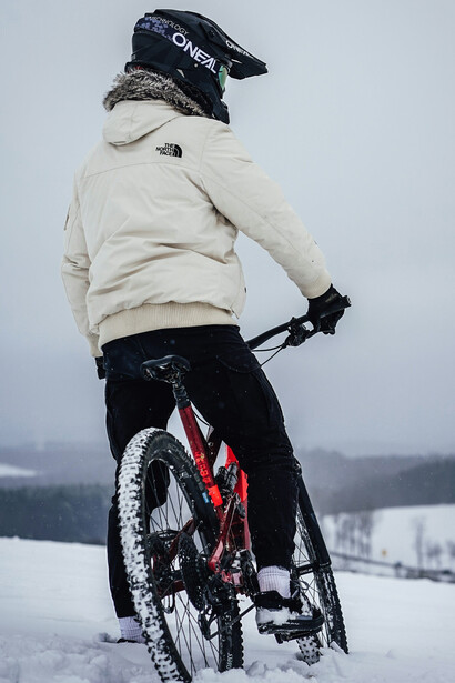 A man in a beige jacket riding a red mountain bike across the snow-covered ground of Jammu & Kashmir, India, during the daytime
