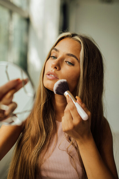 Close-up of a woman holding a makeup brush and mirror as she prepares for the day