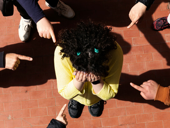 A young person wearing a garment is mocked and pointed at by classmates, experiencing bullying