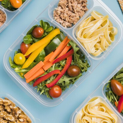 Plastic meal containers filled with vegetables and wraps mirror the organized, performance-focused food service of today's Olympic Villages