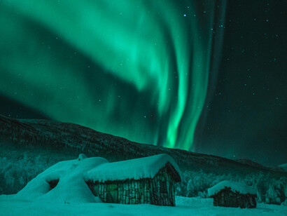 Aurora boreal cubre unas cabañas cubiertas de nieves. La unidad esencial de energía y materia en la filosofía
