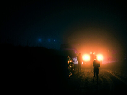 An group of poeple and vehicles backlit by mysterious lights on a moonless night
