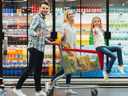 A cheerful young family with their child enjoys a moment together on a shopping cart in a grocery store aisle filled with food products