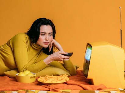 A woman leaning toward a vintage television with remote in hand, reflecting the calming effect of repeat viewing habits