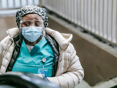 A Black nurse wearing a mask rides the escalator in the underground, unnoticed by the people around her