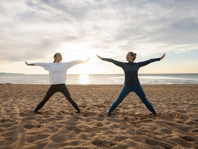 A mother and daughter harmonize in beachside yoga, embodying the essence of familial unity and well-being against a backdrop of sun-kissed shores