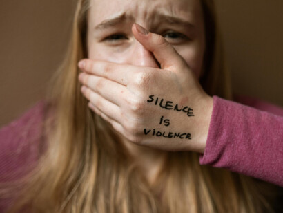 A woman covers her face with her hand, where the words “silence is violence” are written on her palm