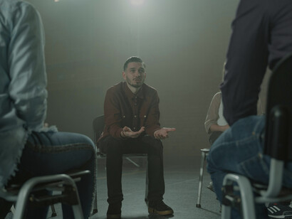 A group therapy session focused on OCD, featuring individuals engaging in discussion and public speaking on mental health