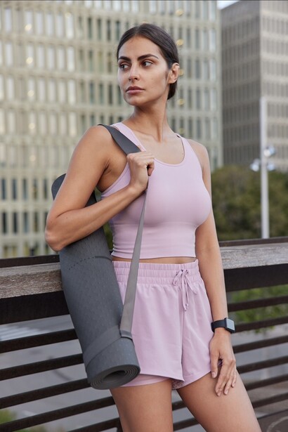 A woman in sportswear carrying a rolled yoga mat and resistance band while listening to motivational music