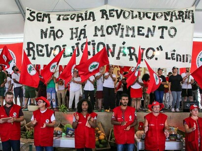 Militantes seguram bandeiras do MST e uma faixa com a frase "Sem teoria revolucionária não há movimento revolucionário. Lênin". O texto debate a necessidade de repensar estratégias e projetos políticos diante das transformações do mundo contemporâneo