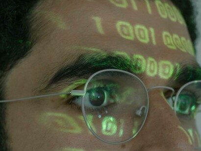A man fixated on his computer screen while a binary code is tattooed on his face