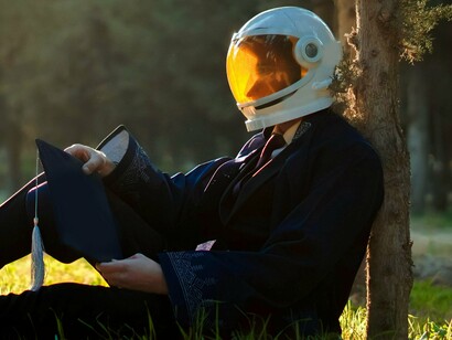 Homem de capacete reflexivo sob uma árvore.  Aqui, a imigração pode ser lida como um resgate necessário, uma busca de significar um vazio, que nos traga paz e nos leve a vibrar em direção à plenitude. É rumar na direção do território que nos traz alento e faz-nos evoluir. Para alguns, essa desconexão com o seu espaço nascituro é ferida profunda. Ela pode manifestar-se em adoecimento físico e emocional. A decisão de voltar ou permanecer é difícil