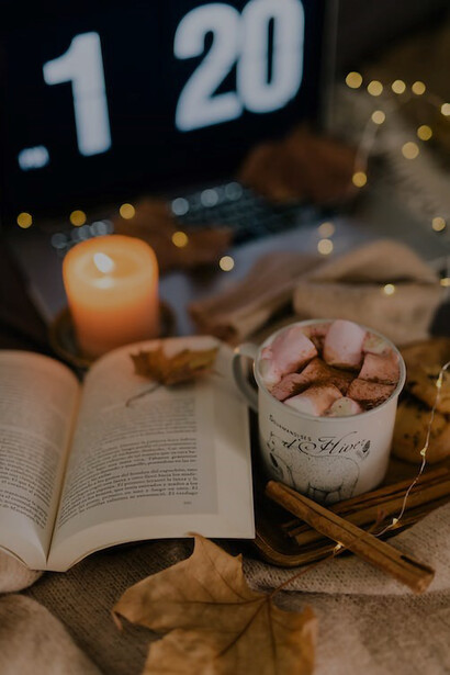 A book lies open beside a flickering candle, casting a warm glow on an autumn evening
