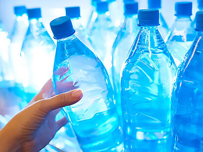 Against the backdrop of water privatization debates, an individual is captured selecting bottled water from a market display, showcasing the increasing demand for packaged solutions amidst concerns over water quality and accessibility