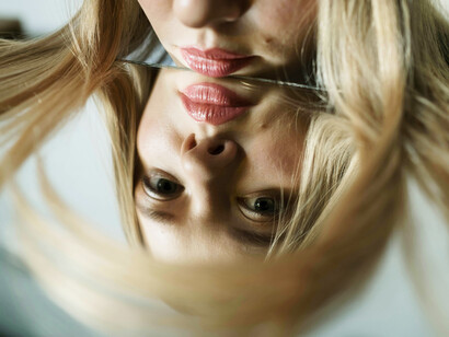 A blonde-haired woman rests her face against a mirror, appearing upset and symbolising hypocrisy