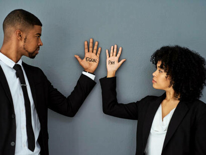 An African American woman and man holding their hands up, each with "equal pay" written on them to support wage equality
