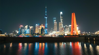 As luzes de Xangai iluminam o horizonte e se refletem nas águas da cidade durante a noite. A moderna paisagem urbana simboliza a retomada do protagonismo econômico chinês discutida ao longo do texto.
