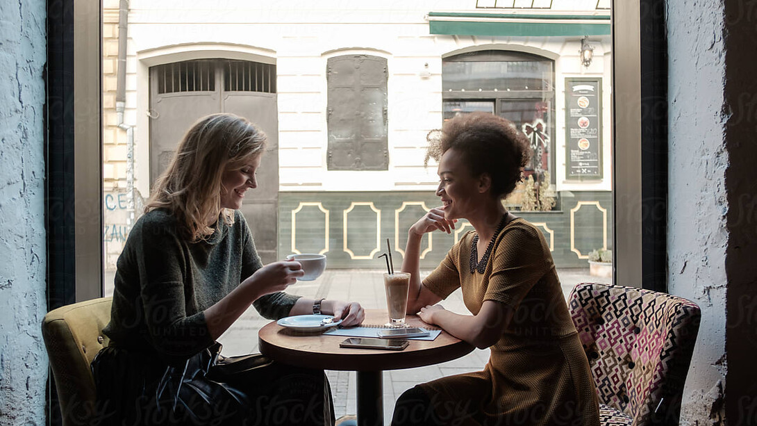 Two women share an emotional reunion in a café, laughing together