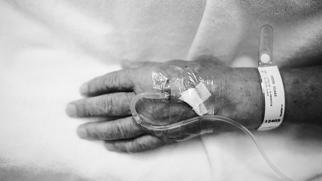 An elderly patient's hand with injections and an IV tube
