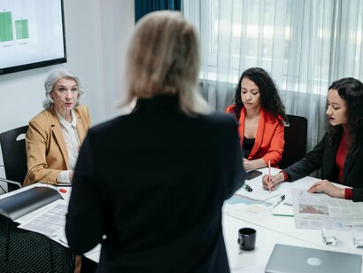 À frente da equipe, uma mulher conduz uma reunião com proximidade e visão, transformando o diálogo em ferramenta de liderança e crescimento coletivo