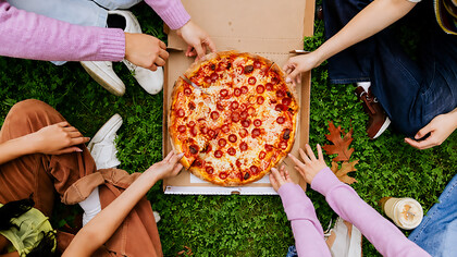 Several hands reaching for a slice of pizza during a picnic, capturing a casual moment of shared food and togetherness