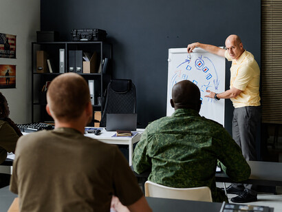 Military trainer presenting battlefield tactics using a whiteboard with hand-drawn sketches and operational arrows