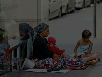 A woman of the Roma group and her children are on the street sitting down and seeking help 