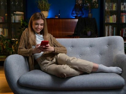 A woman sitting comfortably on her couch at home, engaged with her phone, immersed in the world of digital media and its influence