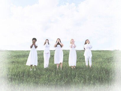Five women, wearing white, standing free in a field covering their eyes
