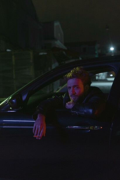 A man looking out the window of a black car at night