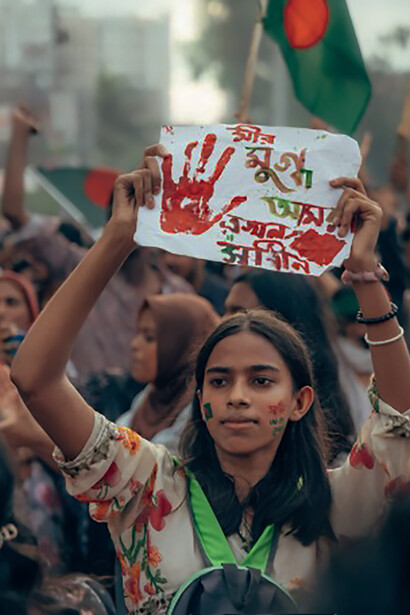 A woman holds up a sign that reads 'We Got Our Pride' amidst a crowd in Cumilla, Bangladesh, symbolizing the region's struggle for unity and identity amidst historical divisions