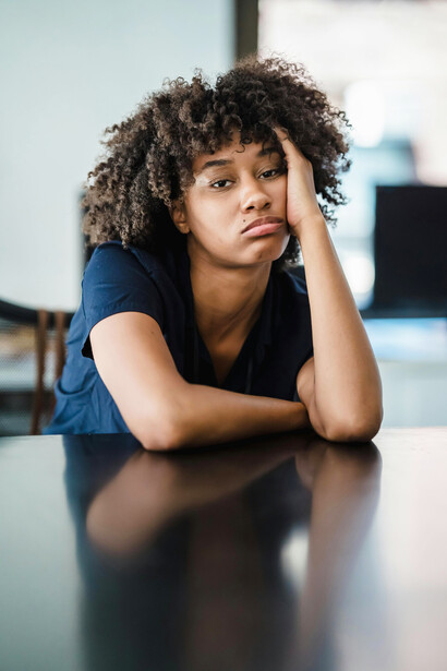 Portrait of a woman sitting at her desk with her hand touching her face, looking tired and deeply thoughtful