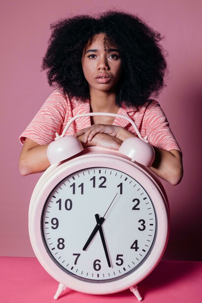 A woman gazing at a large pink alarm clock, symbolizing the passage of time