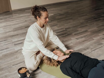 A woman places her hands above her client and attempts to heal her