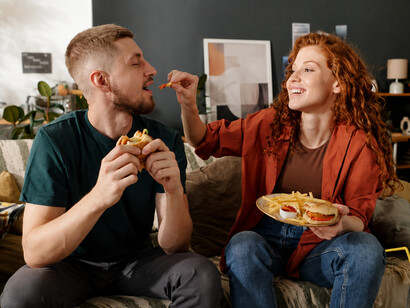 Young couple sharing a meal as the woman looks at her boyfriend’s fast-food plate, symbolizing modern processed food consumption