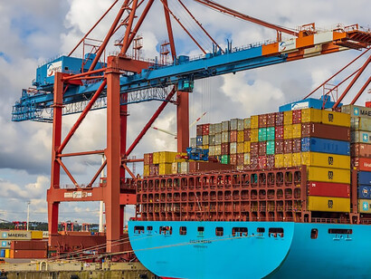 Under the clear daytime skies of Hamburg, Germany, a vibrant blue and red cargo ship navigates the open sea