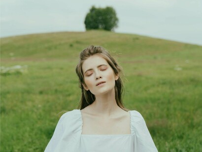 A serene young woman stands in a vast green field, eyes closed, symbolizing the quiet search for understanding amid the noise of the digital age