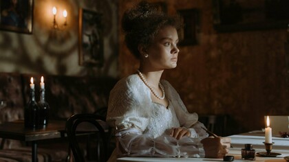 A woman seated in dim candlelight with pen in hand, representing the psychological aftermath of the Spanish flu