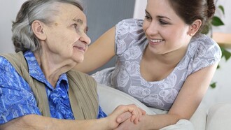Una anciana toma la mano de su cuidadora