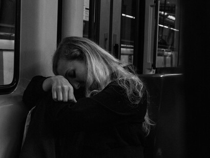 Side view of a woman in a black jacket sitting alone on a subway, looking out the window