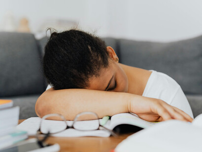 A student wearing a white shirt sits with her hands on her head, reflecting stress and exhaustion