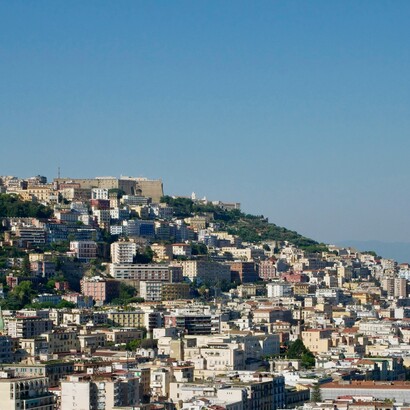 A Napoli, l’ordine razionale dei decumani convive con un intreccio di vicoli, cortili e architetture spontanee che raccontano una città continuamente reinventata dall’abitare popolare. Veduta di Napoli dal Belvedere di San Martino, Italia