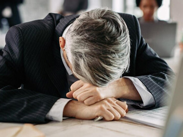 A fatigued businessman slumps over his desk, overwhelmed by the pressures of a toxic workplace, while in the background, stressed and anxious employees face ongoing conflict and burnout